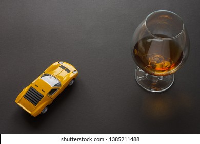Ein Glas Cognac und ein gelbes Metallspielzeug-Sportauto. Stillleben. Dunkler Hintergrund