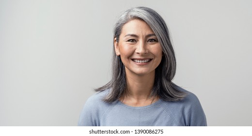 美しい成熟したアジアの女性は、スタジオで広く微笑みます。右側のトーンのクローズ アップの肖像画。白色の背景。