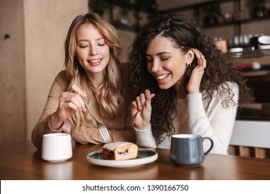 Bild von aufgeregten, glücklichen, hübschen Mädchen, die im Café sitzen und Kaffee trinken, essen Kuchen.