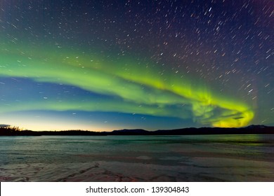 Intens noorderlicht of Aurora borealis of poollicht en ochtenddageraad op de nachtelijke hemel boven het ijzige landschap van het bevroren Lake Laberge Yukon Territory Canada
