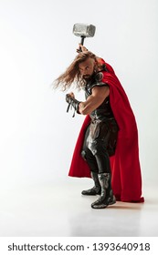 Long hair and muscular male model in leather viking's costume with the big hammer cosplaying isolated on white studio background. Half-lenght portrait. Fantasy warrior, antique battle concept.