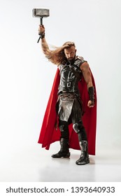 Long hair and muscular male model in leather viking's costume with the big hammer cosplaying isolated on white studio background. Half-lenght portrait. Fantasy warrior, antique battle concept.