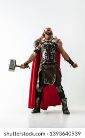 Long hair and muscular male model in leather viking's costume with the big hammer cosplaying isolated on white studio background. Half-lenght portrait. Fantasy warrior, antique battle concept.