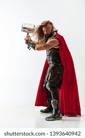 Long hair and muscular male model in leather viking's costume with the big hammer cosplaying isolated on white studio background. Half-lenght portrait. Fantasy warrior, antique battle concept.