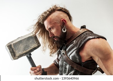 God of thunder. Blonde long hair and muscular male model in leather viking's costume with the big hammer cosplaying isolated on white studio background. Fantasy warrior, antique battle concept.