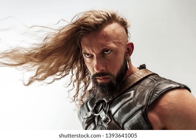 Threatening. Blonde long hair and muscular male model in leather viking's costume with the big hammer cosplaying isolated on white studio background. Fantasy warrior, antique battle concept.