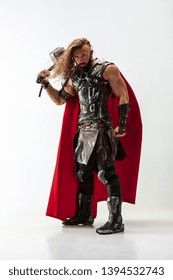 Long hair and muscular male model in leather viking's costume with the big hammer cosplaying isolated on white studio background. Full-lenght portrait. Fantasy warrior, antique battle concept.