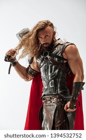 Long hair and muscular male model in leather viking's costume with the big hammer cosplaying isolated on white studio background. Half-lenght portrait. Fantasy warrior, antique battle concept.