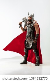 Long hair and muscular male model in leather viking's costume with the big hammer cosplaying isolated on white studio background. Full-lenght portrait. Fantasy warrior, antique battle concept.