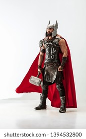 Long hair and muscular male model in leather viking's costume with the big hammer cosplaying isolated on white studio background. Full-lenght portrait. Fantasy warrior, antique battle concept.