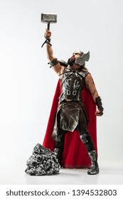 Long hair and muscular male model in leather viking's costume with the big hammer cosplaying isolated on white studio background. Full-lenght portrait. Fantasy warrior, antique battle concept.