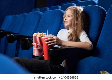 Zijaanzicht van een knappe tiener die heerlijke popcorn eet en koolzuurhoudend zoet water drinkt in de bioscoop. Een lachend meisje zit alleen in de hal en kijkt naar een komische film. Concept van entertainment.