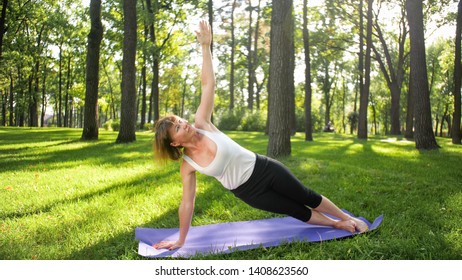 Billede af smilende glad kvinde på 40 år laver yogaøvelser på fitnessmåtte i skoven. Harmoni af menneskelig natur. Midaldrende mennesker tager bilen af ​​mental og fysisk sundhed