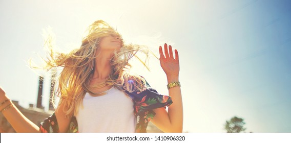 Atractiva mujer joven feliz con camiseta blanca que vuela el pelo disfrutando de su tiempo libre al atardecer al aire libre. Retrato de chica rubia de belleza en verano. Concepto de primavera de estilo de vida de libertad. resplandor del sol en el fondo