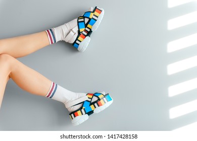 Beautiful female legs in white trendy socks posing in colorful fashionable high wedge leather sandals on gray background. Asian anime style concept. Womens legs wearing high sole summer stylish shoes