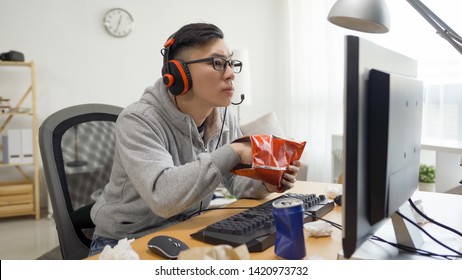 アジアの中国人男性の手は、コンピューターゲームで楽しい余暇を過ごしながら、ソーダでファーストフードバッグポテトチップスを食べることができます。不健康なジャンク フード ライフ スタイル コンセプト。オタク アニメ 夏休み