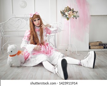 Beautiful girl in the image of a doll sitting on the floor in a bright interior. Studio photography . Girl-loli in a pink dress and white tights. Cosplay, Anime, Harajuku