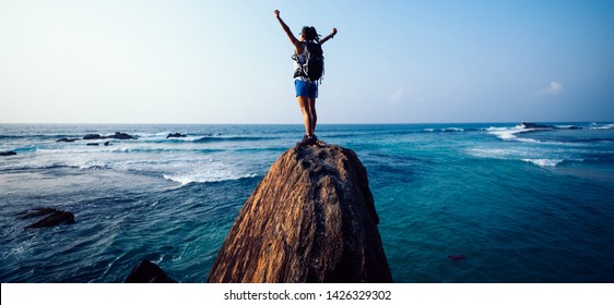 Succesvolle jonge vrouw wandelaar uitgestrekte armen op de rand van de rotsklif aan zee