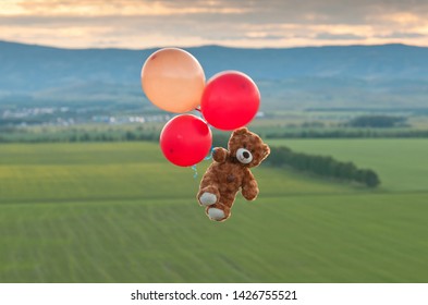 Oso de peluche volando hacia el cielo con grandes globos amarillos y rojos. El oso volando sobre los campos.