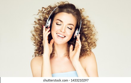 Mooi lachend meisje met klein krullend haar luisteren naar muziek. Vrolijke vrouw in grote koptelefoon genieten van het leven. Afro volumineus kapsel