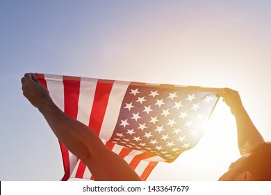 アメリカ合衆国の独立記念日。澄んだ青い空にアメリカ国旗を振って手を上げた男性の低角度のビュー。アメリカの愛国心の概念