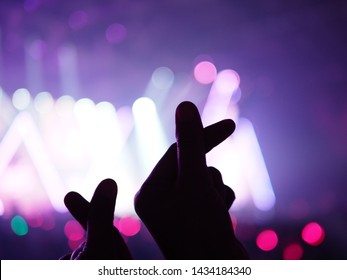 K-Pop müzik teması veya Canlı konser arka planı, sahnenin bulanık arka planında ışık efektleriyle sanatçıya destek veren izleyicilerin silüet ellerinin mini kalp şeklinde el hareketi yapmasıyla.