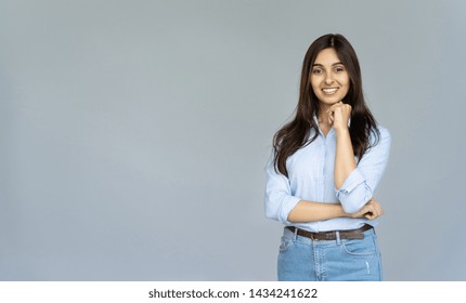 Lächelnde indische junge Geschäftsfrau trägt blaues Jeanshemd und blickt in die Kamera isoliert auf grauem, leerem Studiohintergrund mit Kopierraum, glückliche hübsche hinduistische Studentin posiert auf grauer Wand, Porträt