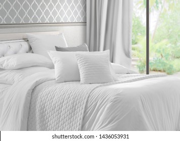 Luxury bedroom that opens with French doors onto a terrace. King bed with white linens and pillows. Interior with garden view window, bed with white bed linen and curtains.