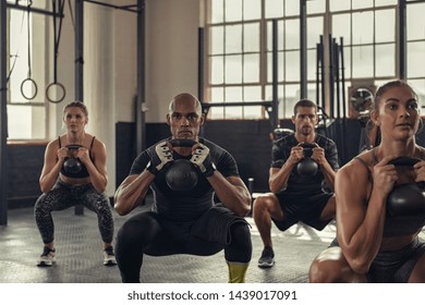 Fitness vrouwen en vastberaden mannen trainen met kettlebell op sportschool. Groep jongeren die een kettlebell-oefening doen met hurken. Multi-etnische groep die hurkoefening doet terwijl ze gewicht vasthoudt.