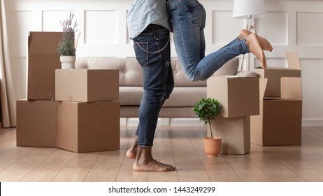 Close up young husband in jeans lift wife surrounded by cardboard boxes excited to move in new flat, happy african American couple have fun hug feel euphoric relocating together to own house
