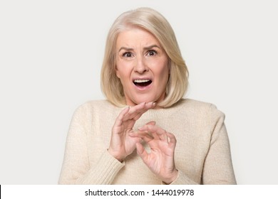 Elderly woman standing frozen very scared pushing off with hands. Old female being afraid of something, frightened looking at camera with disgust. Lady studio portrait isolated on gray background