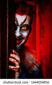 A close up portrait of an angry clown from a horror film hiding behind a door. Halloween, carnival.