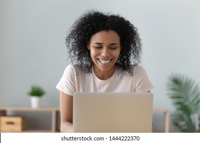 Cheerful african black girl student laughing read good internet news or watching funny online show feel happy get great exam results having fun enjoy comedy movie sit at home office desk with laptop