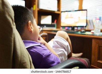 Asian black short-haired boy photos wearing a purple shirt sitting watching a cartoon on the screen