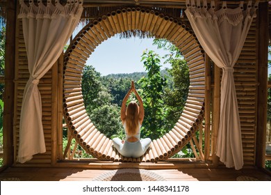 Young girl doing yoga outdoor. Young woman practicing yoga in bamboo house, nature on background.Female happiness.Caucasian woman practicing yoga on vacation on Bali island