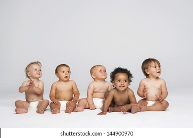 Hàng em bé đa sắc tộc ngồi cạnh nhau nhìn ra xa bị cô lập trên nền xám