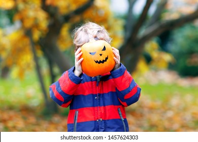 Happy cute little kid boy with halloween pumpkin lantern. Funny child in colorful clothes having fun and playing in autumn garden on cold autumnal day. Scary jack-o-lantern, celebration of holiday.