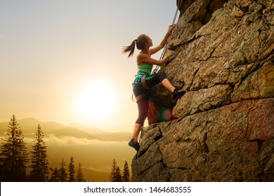 Mooie vrouw klimmen op de hoge rots bij mistige zonsondergang in de bergen. Avontuur en Extreme Sport Concept