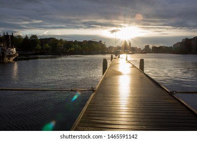 Holzpier mit Booten bei Sonnenuntergang im Amsterdamer Dock. Amsterdamer Stadtschattenbilder im Abenddämmerungslicht. Kathedralenschattenbild am Abendhimmel in den Niederlanden. Innenstadt in Amsterdam Dock.
