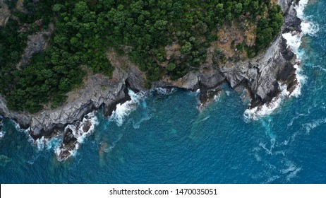 Luchtfoto van rotsachtige bergachtige kust met groene bomen en blauwe zee met witte schuimende golven