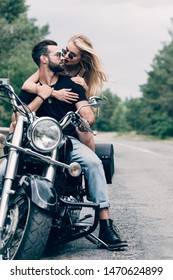 giovane coppia di motociclisti che si guardano da vicino su una motocicletta nera sulla strada vicino alla foresta verde