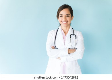 Smilende kvindelig læge i laboratoriefrakke med arme krydset mod blå baggrund