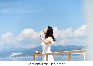 side view of a young asian woman standing by sea looking up at blue sky