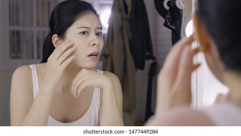 アジアの女性モデルは、化粧台の鏡で顔のにきびや傷跡の問題を見たときにショックを受けました. 女性の顔ににきびと問題のある肌の概念的なショット。舞台裏の楽屋で顔をしかめている女の子