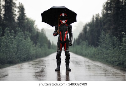 Motorcyklist i fuld gear og hjelm med paraply i regnen. Motorcyklist i de mørke skove.
