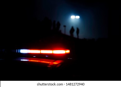Polizeilichter blinken, während Menschen im Hintergrund silhouettiert werden, während eine Straßenlaterne von oben leuchtet.