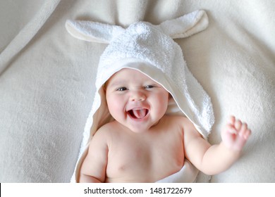 Em bé sơ sinh đáng yêu được quấn bởi khăn lông thỏ trắng với khuôn mặt tươi cười. Cậu bé lai châu Á-Đức hạnh phúc lau khô người sau khi tắm