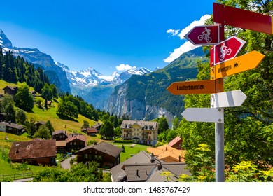 Señal de carretera con flechas para rutas turísticas de senderismo y ciclismo que apuntan a la bifurcación en la carretera desde el pueblo de Wengen hasta Lauterbrunnen, Oberland bernés, Suiza. El Jungfrau es visible en el fondo