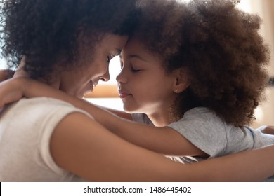 クローズ アップ ヘッド ショット側ビュー穏やかな幸せな混血の母は、小さなかわいい娘を抱きしめて、額に触れます。優しい瞬間 家族のサポート、許し、理解。里親を抱きしめる養子。