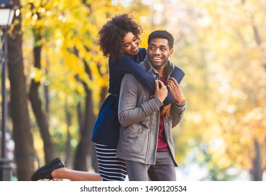 Cute african american girl jumped on boyfriend back, having fun while walking by autumn forest, copy space